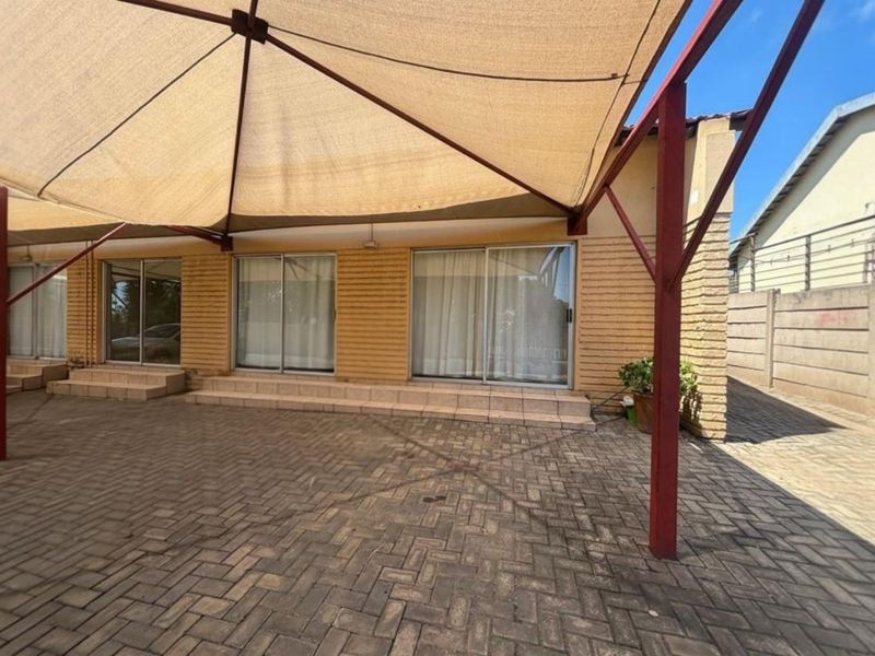Spacious paved outdoor patio area featuring a large shade sail structure and multiple sliding glass door access points to the main dwelling.