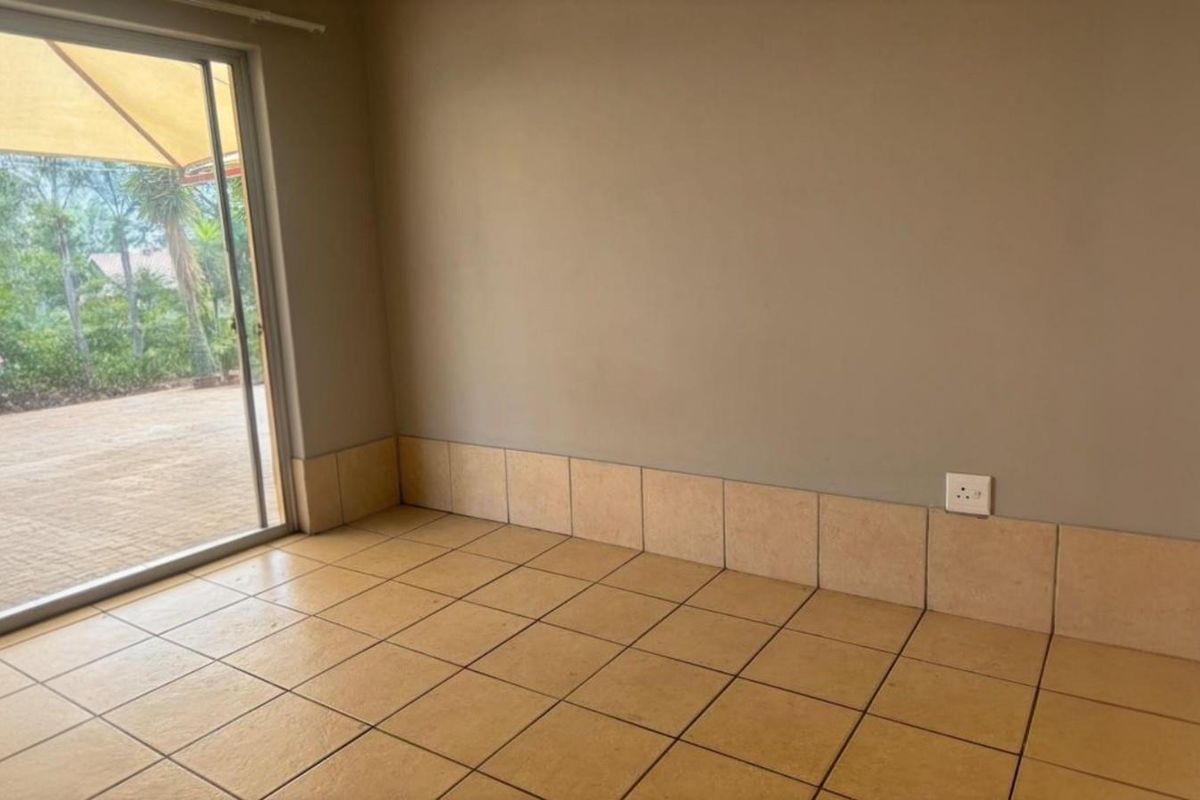 An empty living area featuring ceramic floor tiles, tiled skirting, and a large sliding glass door providing access to the outdoor patio.