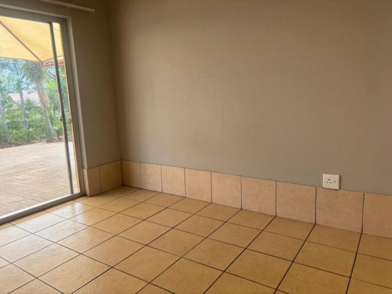 An empty living area featuring ceramic floor tiles, tiled skirting, and a large sliding glass door providing access to the outdoor patio.