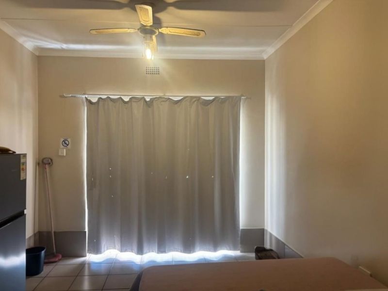 A simple bedroom featuring tiled flooring and a ceiling fan, providing a functional space with neutral wall finishes.