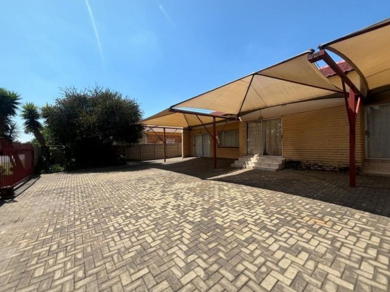Spacious rear paved courtyard featuring a large shade sail structure, brick exterior walls, and direct access to the home via sliding glass doors.