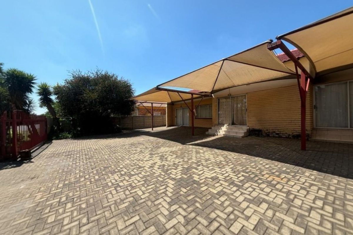 Spacious rear paved courtyard featuring a large shade sail structure, brick exterior walls, and direct access to the home via sliding glass doors.