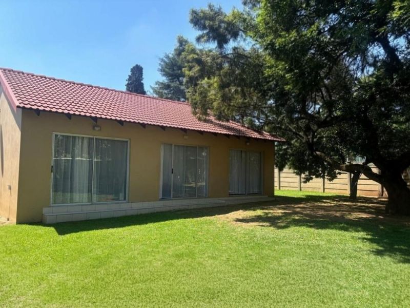 Rear view of the house featuring a tiled roof, plastered exterior walls, and multiple sliding glass doors opening onto a spacious garden area.