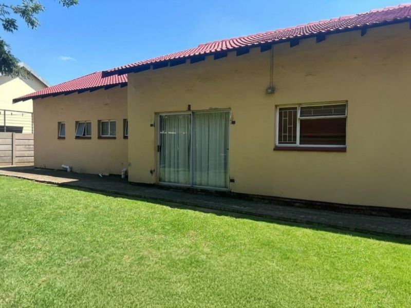 Rear view of the house featuring a red tiled roof, sliding glass doors, and a paved walkway leading to a spacious lawn and boundary wall.
