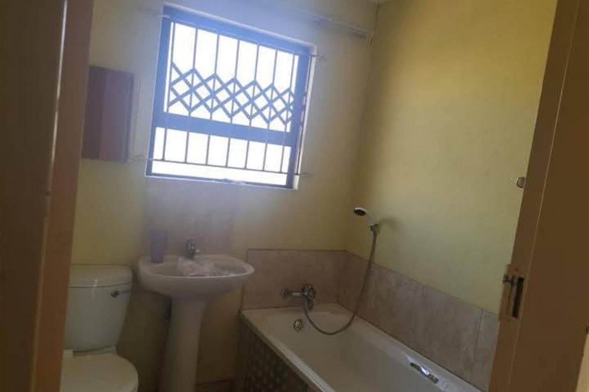 A functional bathroom featuring a pedestal basin, a bathtub with a handheld shower attachment, and a window with security bars.