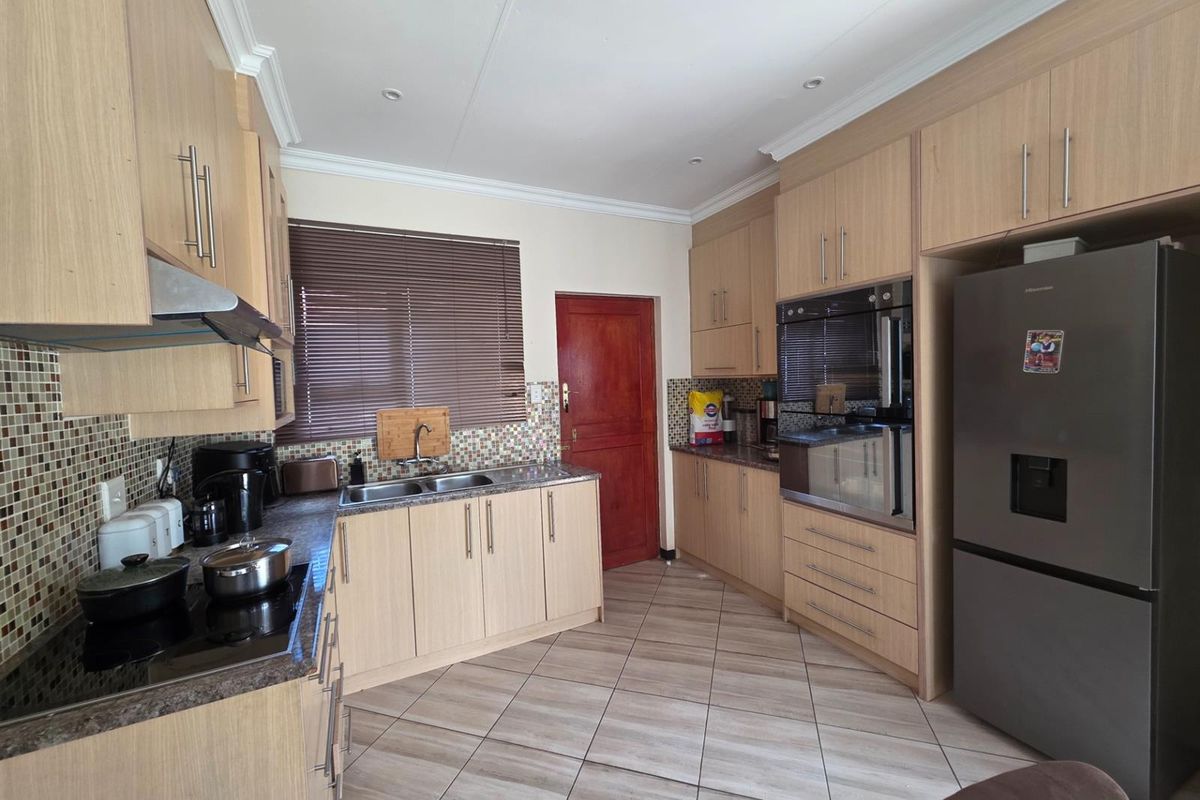 Functional kitchen featuring light wood cabinetry, integrated oven, glass cooktop, double sink, and tiled flooring with a mosaic backsplash.