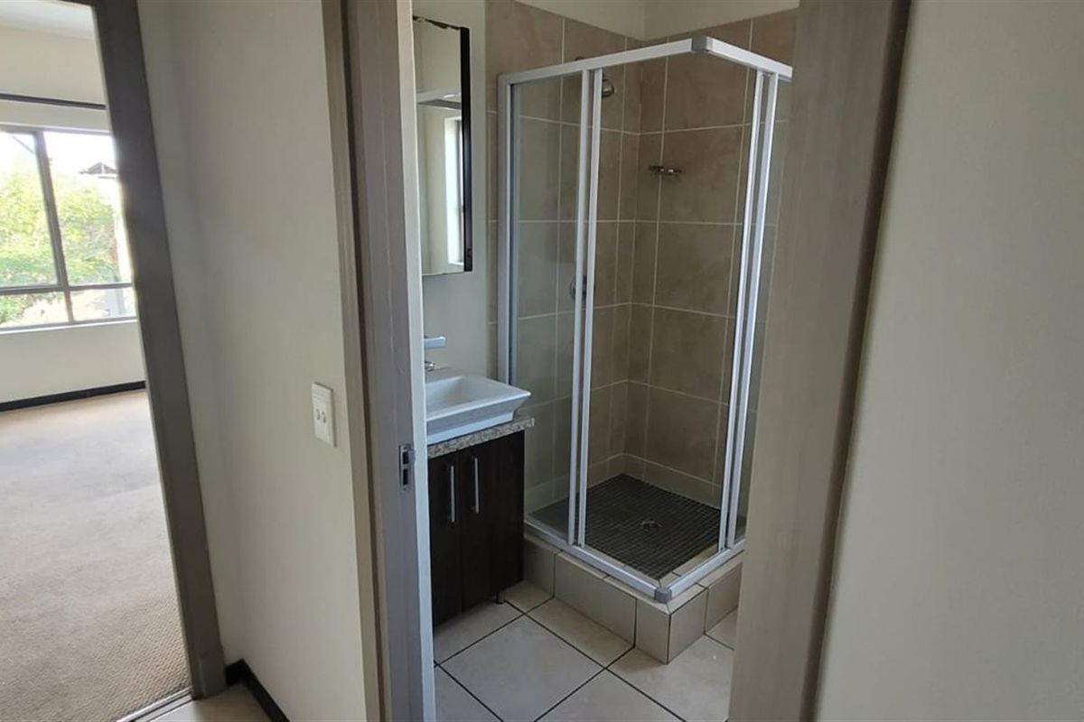 A functional bathroom featuring a shower enclosure, vanity cabinet with basin, and neutral tiled finishes, viewed from the adjacent bedroom area.