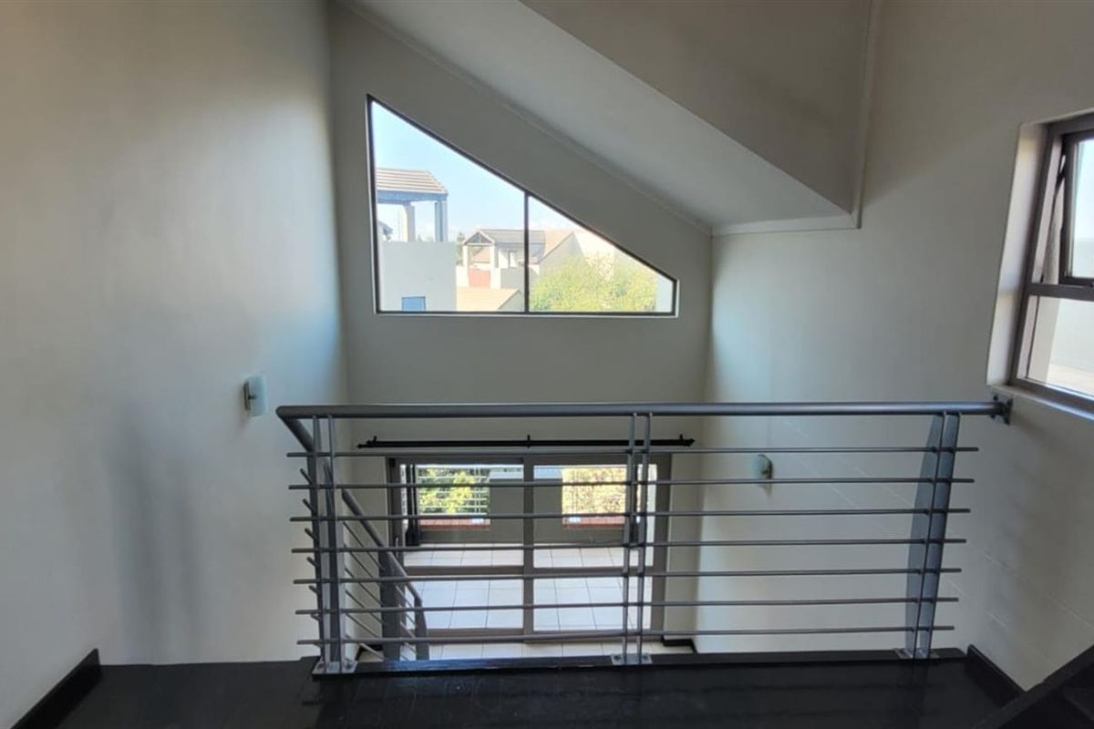 A bright, modern hallway featuring a metal balustrade, a unique triangular window, and a staircase overlooking the lower level.