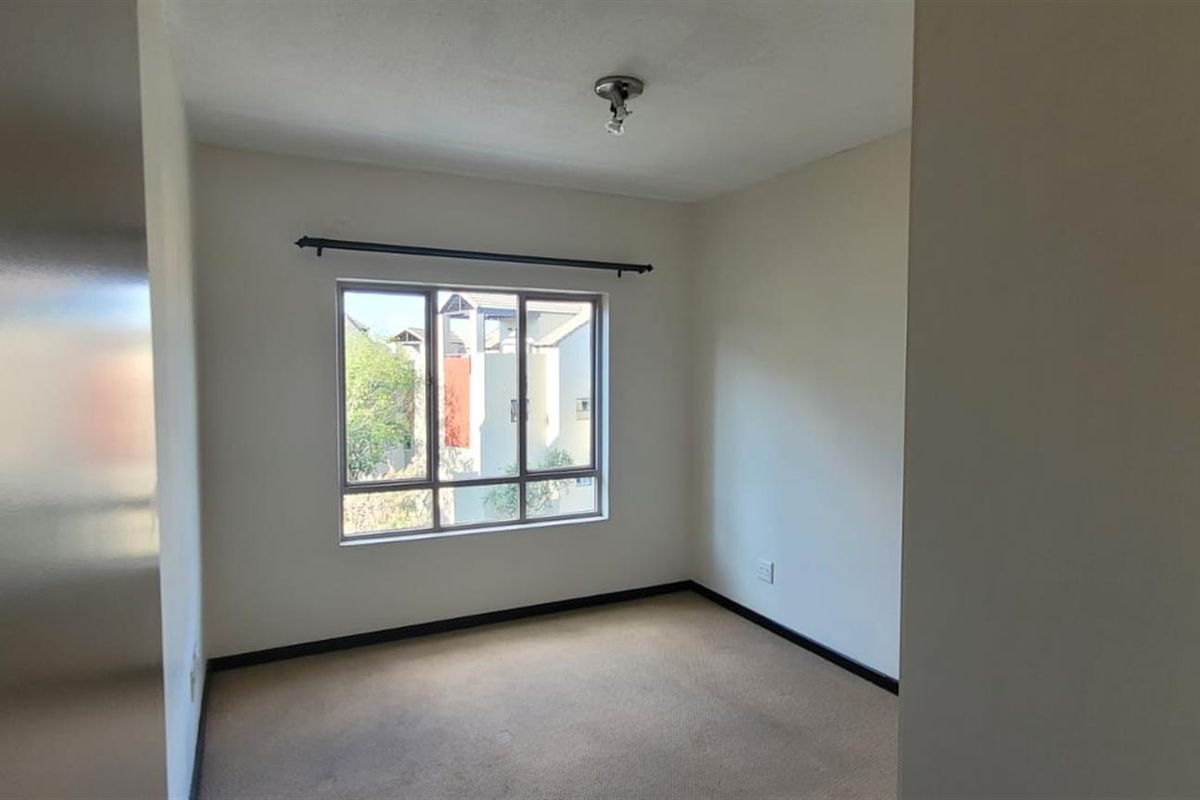 A vacant bedroom featuring neutral walls, carpeted flooring, and a window with a curtain rod, offering a blank canvas for personalization.