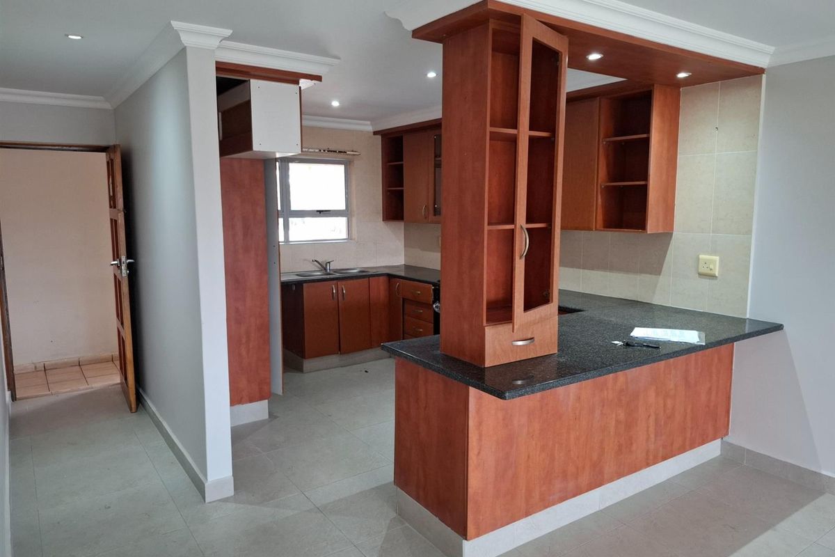 A functional kitchen featuring wooden cabinetry, dark granite countertops, a breakfast bar, and recessed ceiling lighting in an open-plan layout.