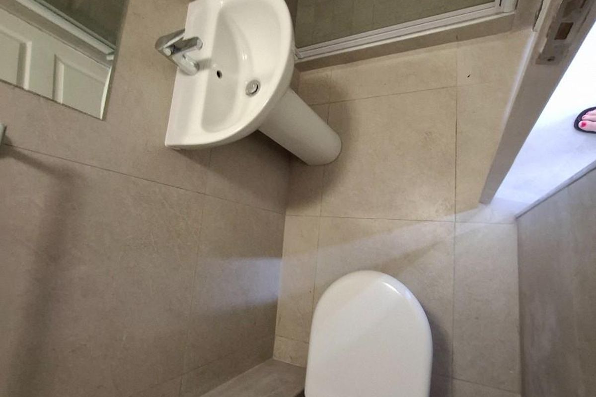A compact, modern bathroom featuring neutral wall tiles, a pedestal basin, a toilet, and a glass-enclosed shower area.