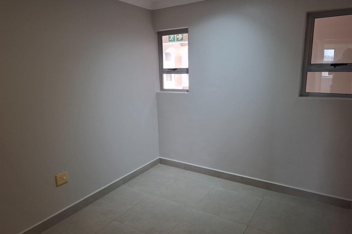 A clean, empty bedroom featuring neutral tiled flooring, light grey walls, and two aluminium-framed windows providing natural light.