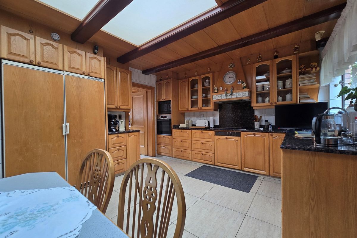 A traditional kitchen featuring extensive timber cabinetry, integrated appliances, granite countertops, and a large skylight providing natural light.