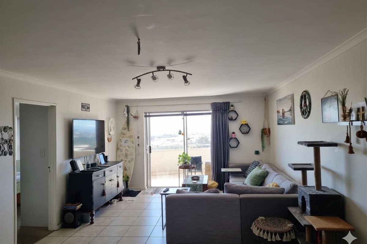 A spacious living room featuring tiled flooring and a sliding glass door providing access to the balcony and natural light.