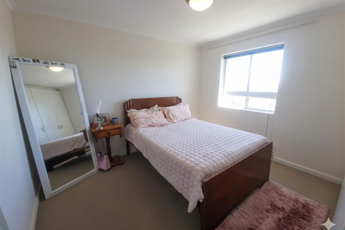 A functional bedroom featuring built-in cupboards, neutral carpeted flooring, and a window allowing for natural light.
