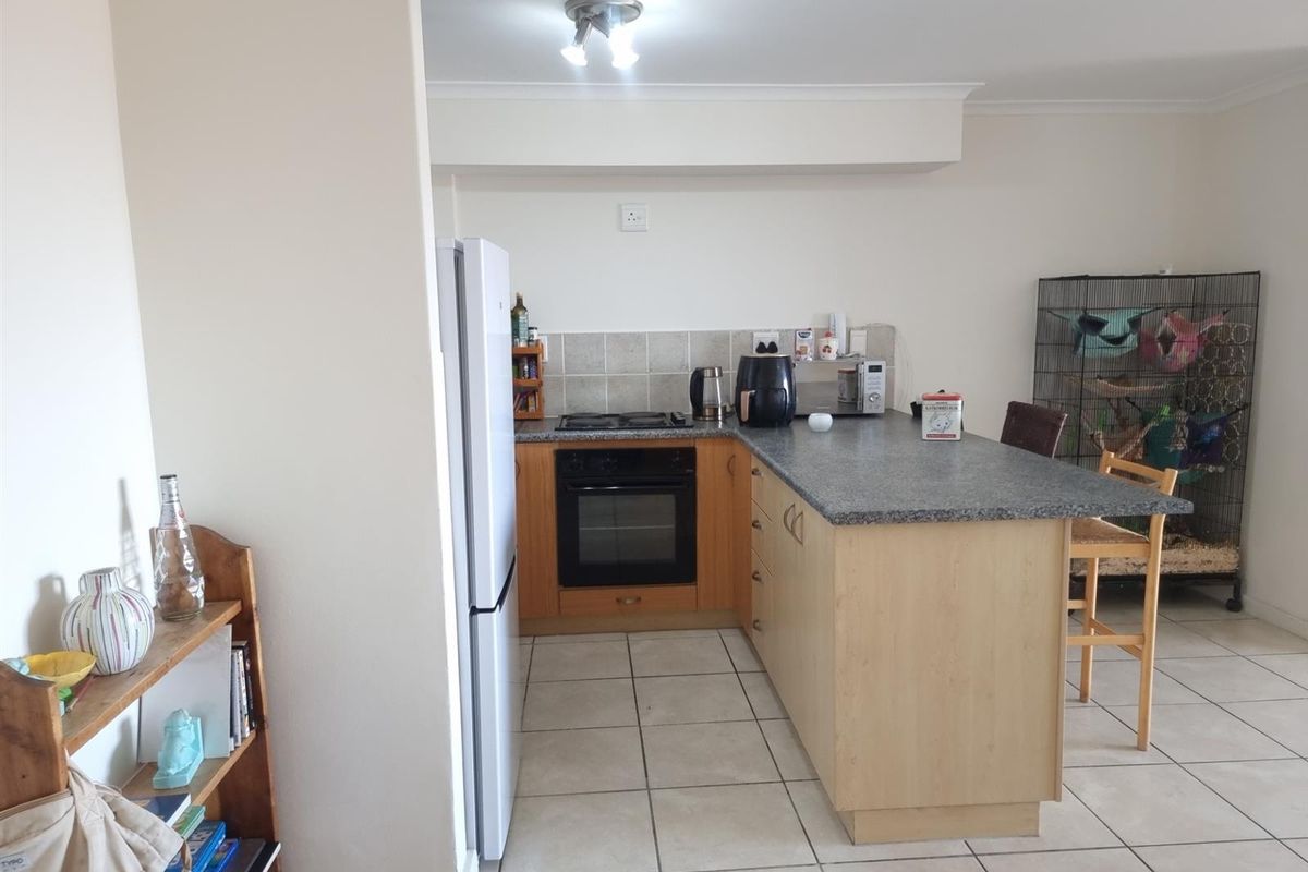 A functional kitchen featuring light wood cabinetry, granite countertops, a gas hob, built-in oven, and tiled flooring with a breakfast bar area.