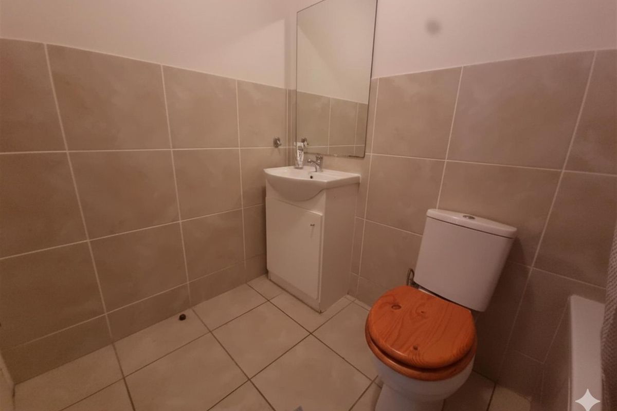 A functional bathroom featuring neutral wall and floor tiling, a vanity cabinet with basin, and a wall-mounted mirror.