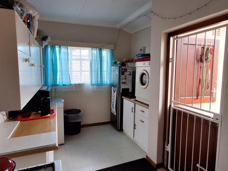 A functional laundry or scullery area featuring built-in cabinetry, tiled flooring, and direct access to the exterior via a security gate.