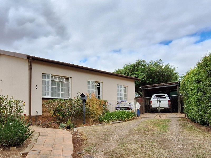Front exterior view of a single-story house featuring a paved walkway, established garden, and a covered carport area.