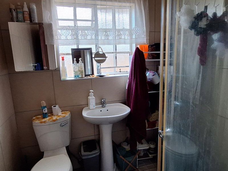 A functional bathroom featuring a pedestal basin, toilet, and a glass-enclosed shower with neutral wall tiling.