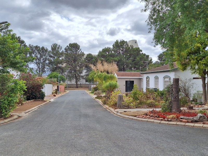A view of a quiet residential street featuring paved roads, mature trees, and established garden landscaping surrounding the property.