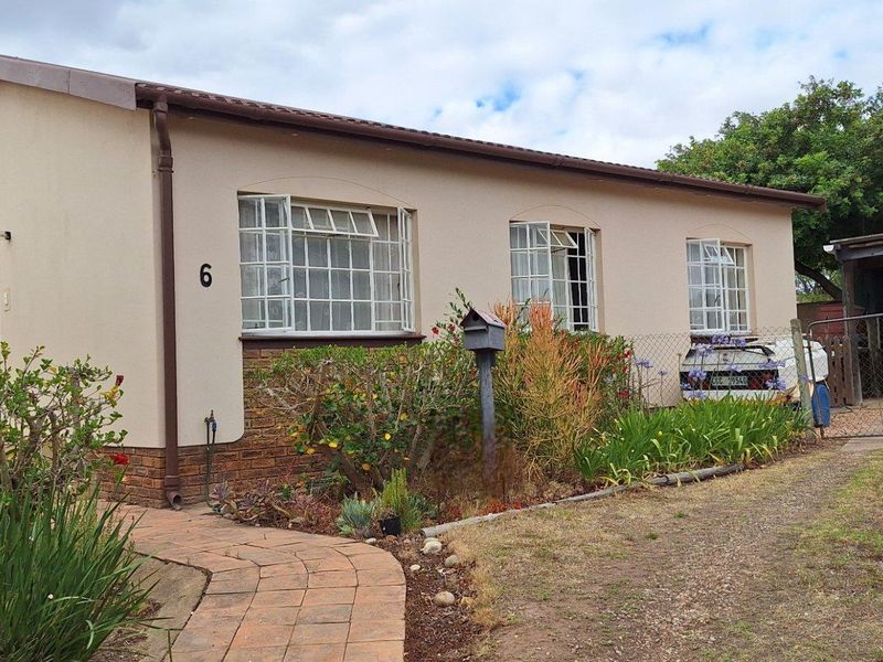 Single-story residential home featuring a paved walkway, established garden, and a side carport with a gated driveway.