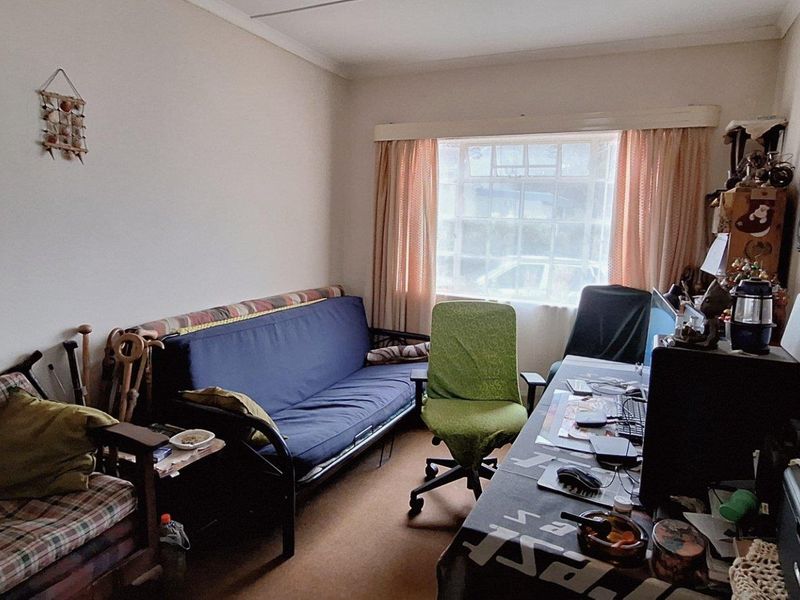 A functional room currently utilized as a home office and living space, featuring carpeted flooring and a large window with curtain tracks.