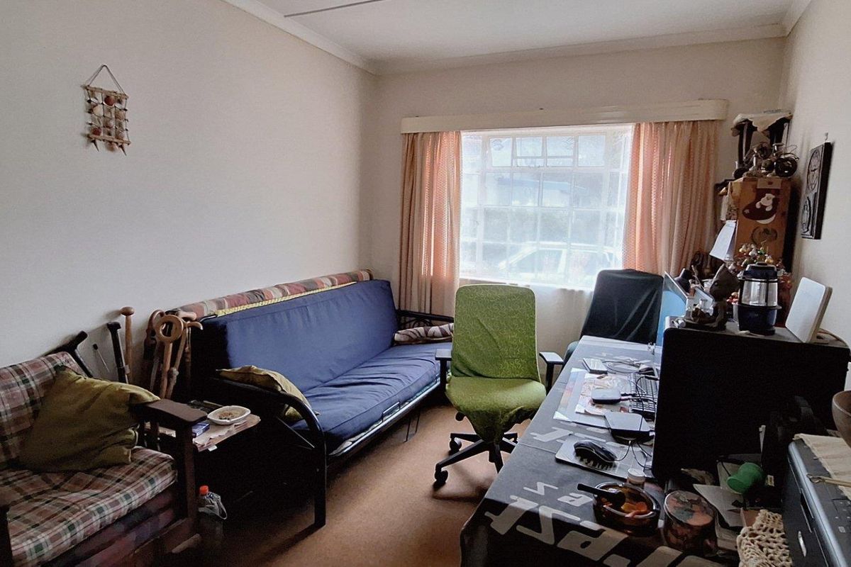 A functional room currently utilized as a home office and living space, featuring carpeted flooring and a large window with curtain tracks.