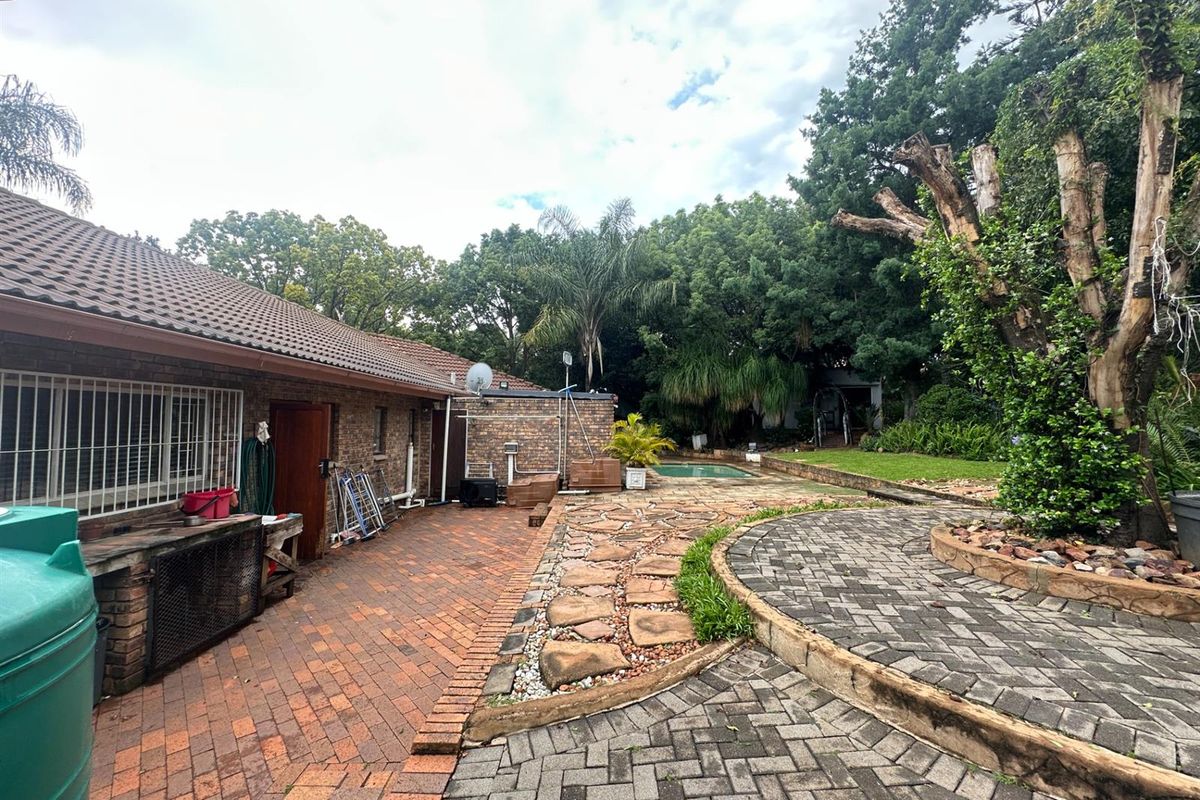 Rear exterior view featuring a brick-paved patio area, established garden, and a swimming pool in the background.
