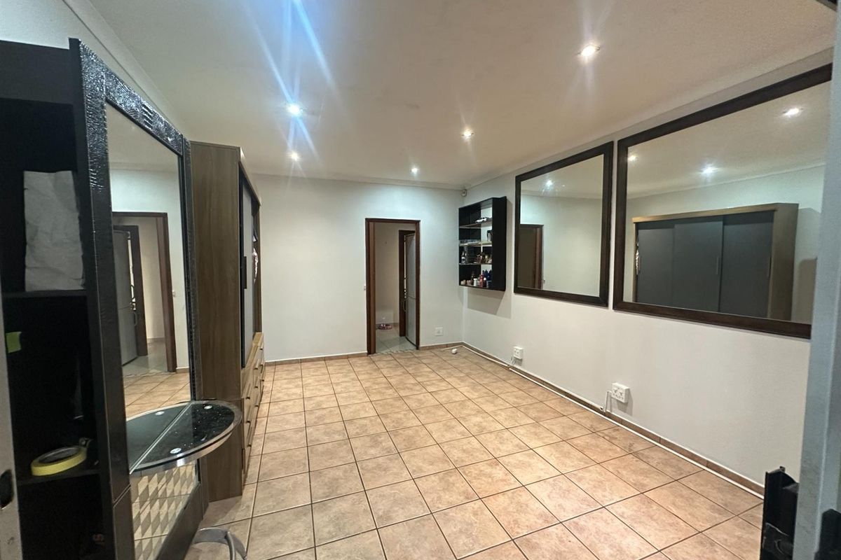 A spacious room featuring tiled flooring, recessed ceiling lighting, and large wall-mounted mirrors, suitable for use as a bedroom or versatile living space.