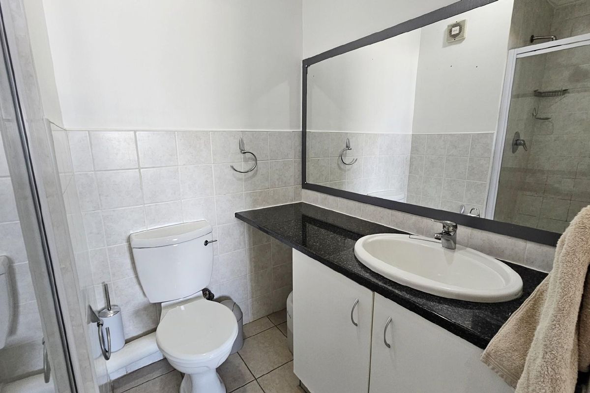 Functional bathroom featuring a granite-topped vanity with integrated basin, large wall mirror, toilet, and a tiled shower enclosure.