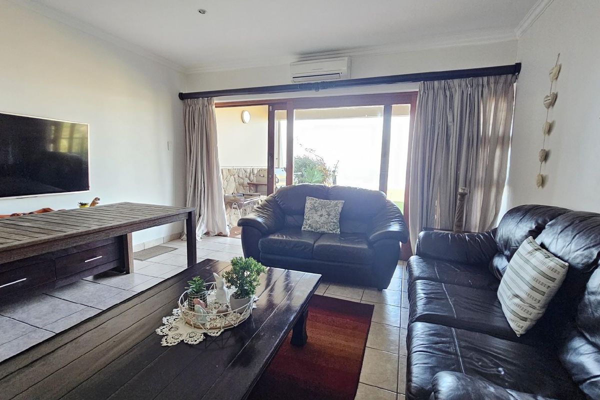 Spacious living room featuring tiled flooring, a wall-mounted air conditioning unit, and large sliding glass doors providing access to an outdoor patio area.