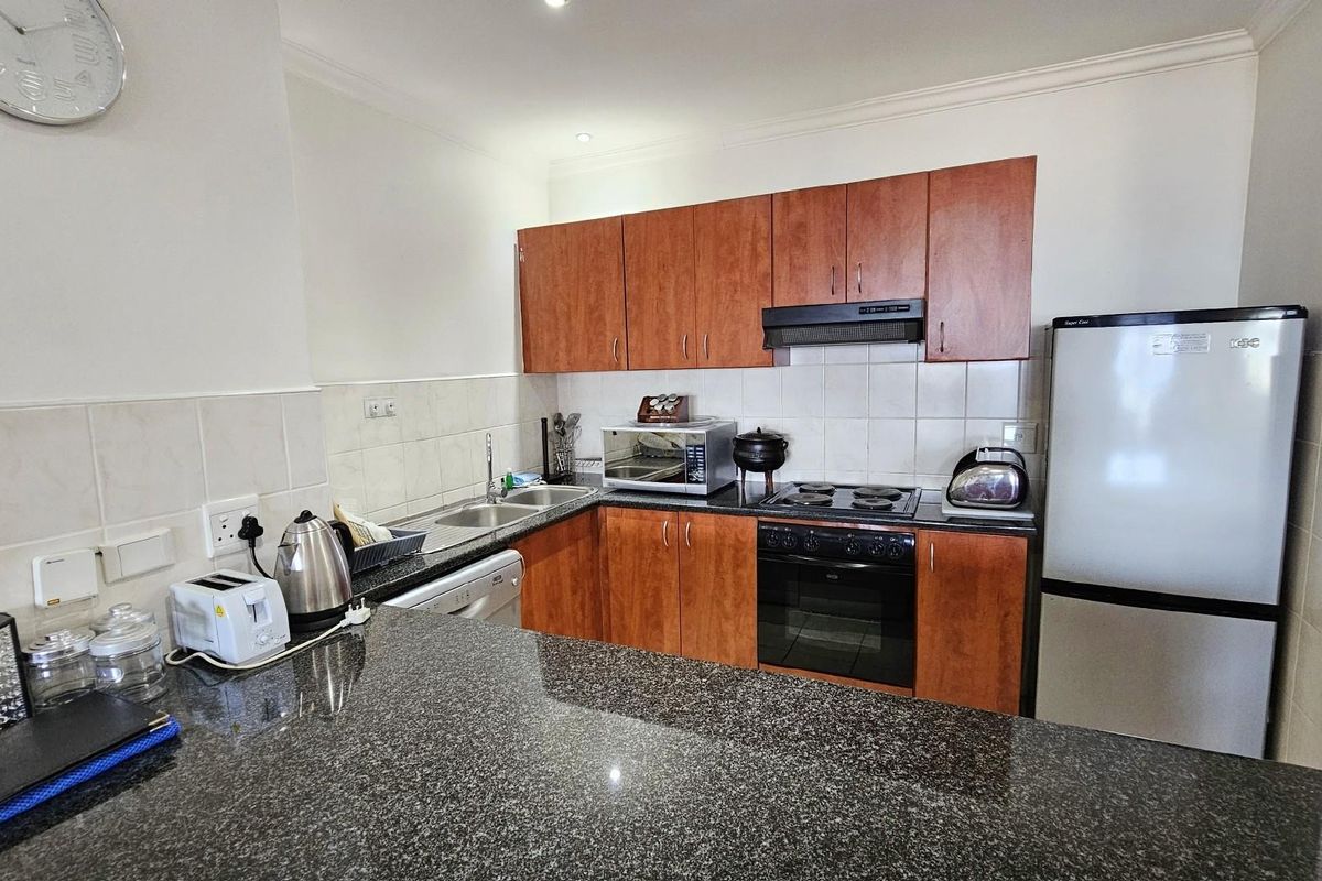 A functional kitchen featuring dark granite countertops, wooden cabinetry, a built-in oven, and a hob with an extractor fan.