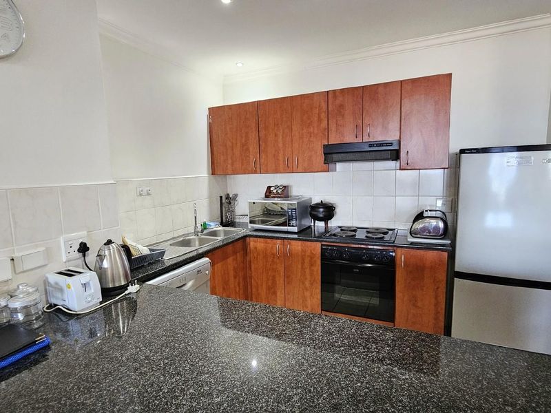 A functional kitchen featuring dark granite countertops, wooden cabinetry, a built-in oven, and a hob with an extractor fan.