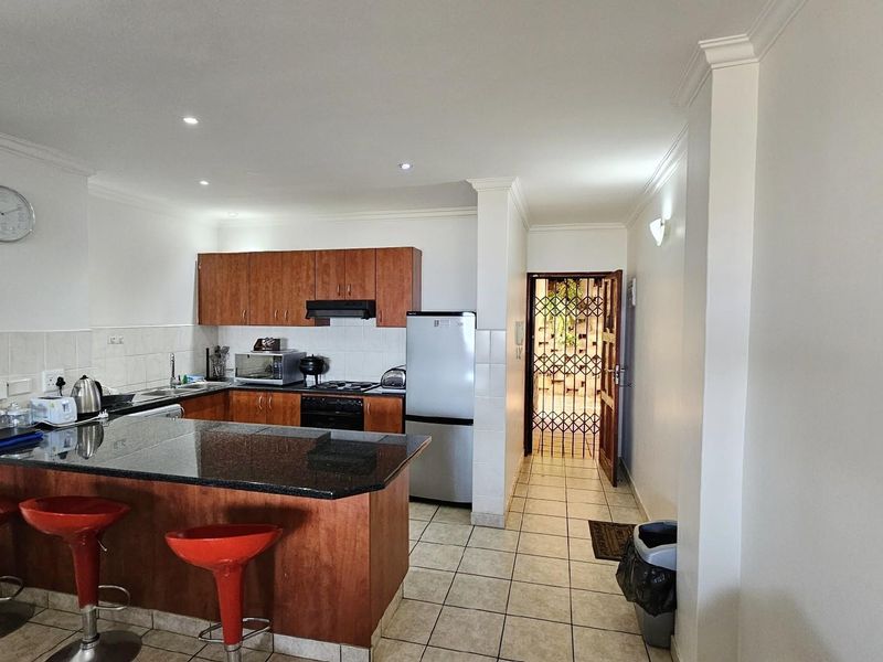 Open-plan kitchen featuring wooden cabinetry, granite countertops, a breakfast bar, and tiled flooring, leading to an entrance with a security gate.