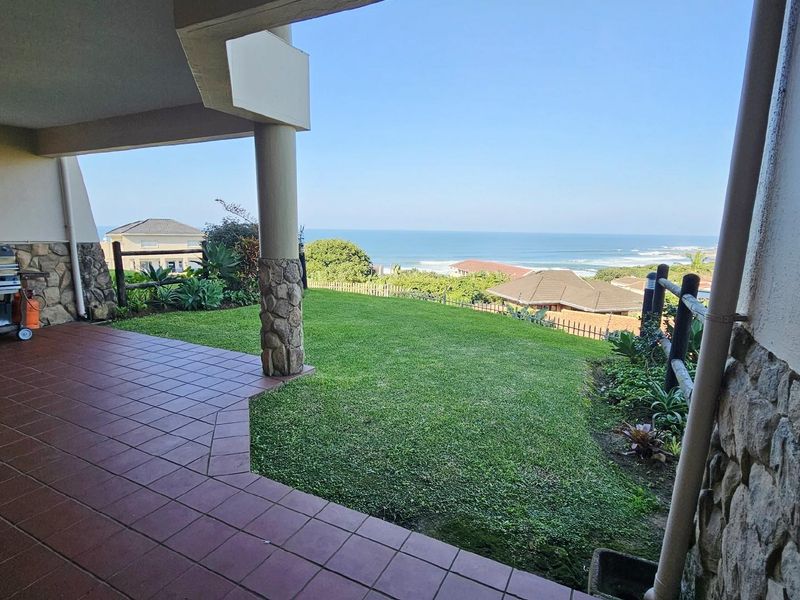 Covered patio area with tiled flooring and stone-clad pillars, overlooking a private garden with expansive ocean views.