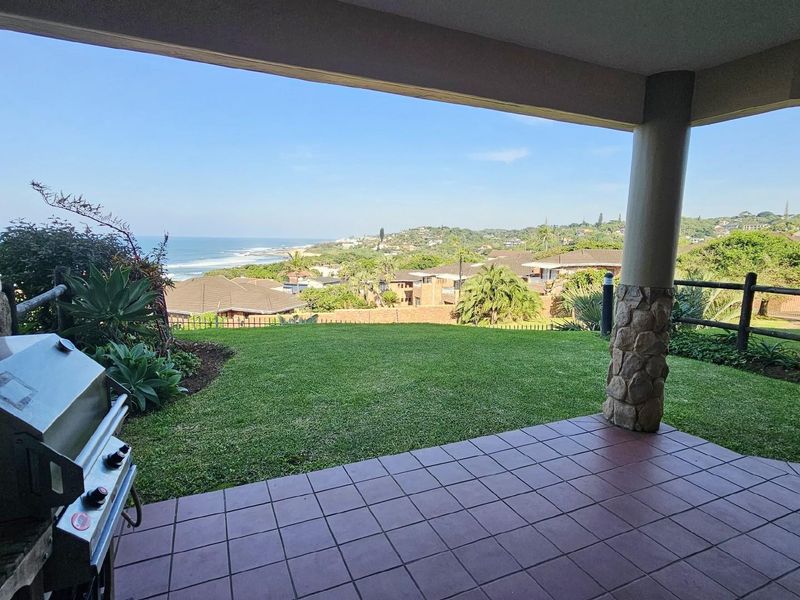 Covered patio featuring tiled flooring and stone-clad support columns, offering expansive coastal and neighborhood views.