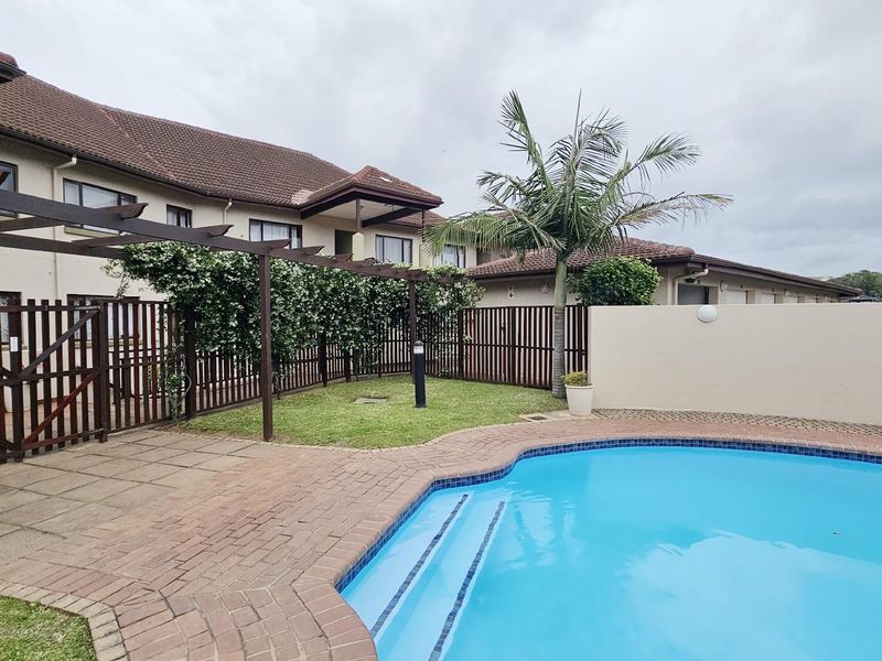 A private outdoor pool area featuring a paved surround, a wooden pergola, and a small lawn area set against the apartment building exterior.