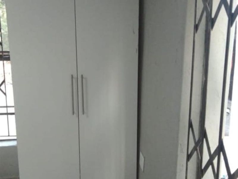 A bedroom space featuring a white built-in wardrobe and a metal security gate on the window.
