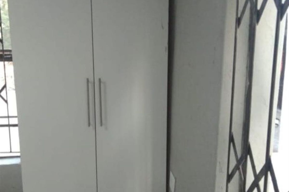 A bedroom space featuring a white built-in wardrobe and a metal security gate on the window.