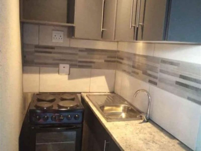 Compact kitchen featuring dark cabinetry, a laminate countertop, stainless steel sink, and a freestanding stove with a tiled backsplash.