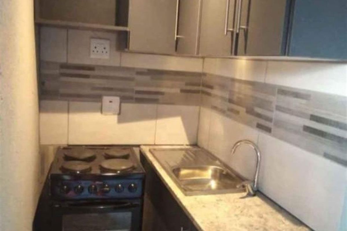 Compact kitchen featuring dark cabinetry, a laminate countertop, stainless steel sink, and a freestanding stove with a tiled backsplash.