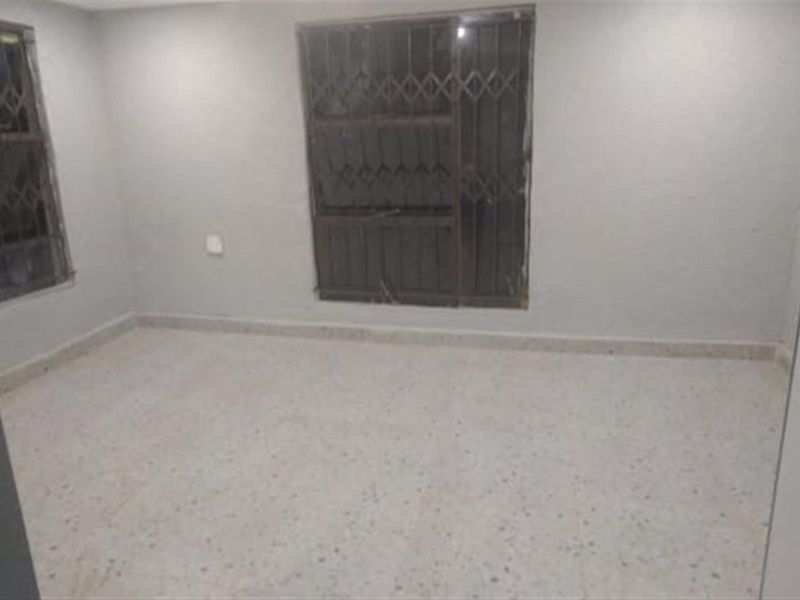 An empty bedroom featuring terrazzo flooring and windows fitted with security gates, offering a blank canvas for renovation.