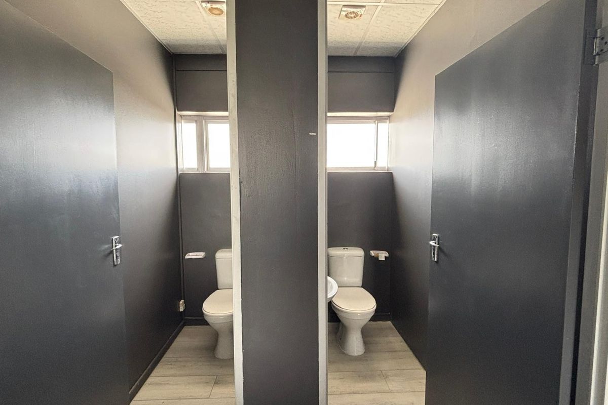 A commercial restroom facility featuring two separate toilet cubicles with dark painted walls, tiled flooring, and integrated lighting.