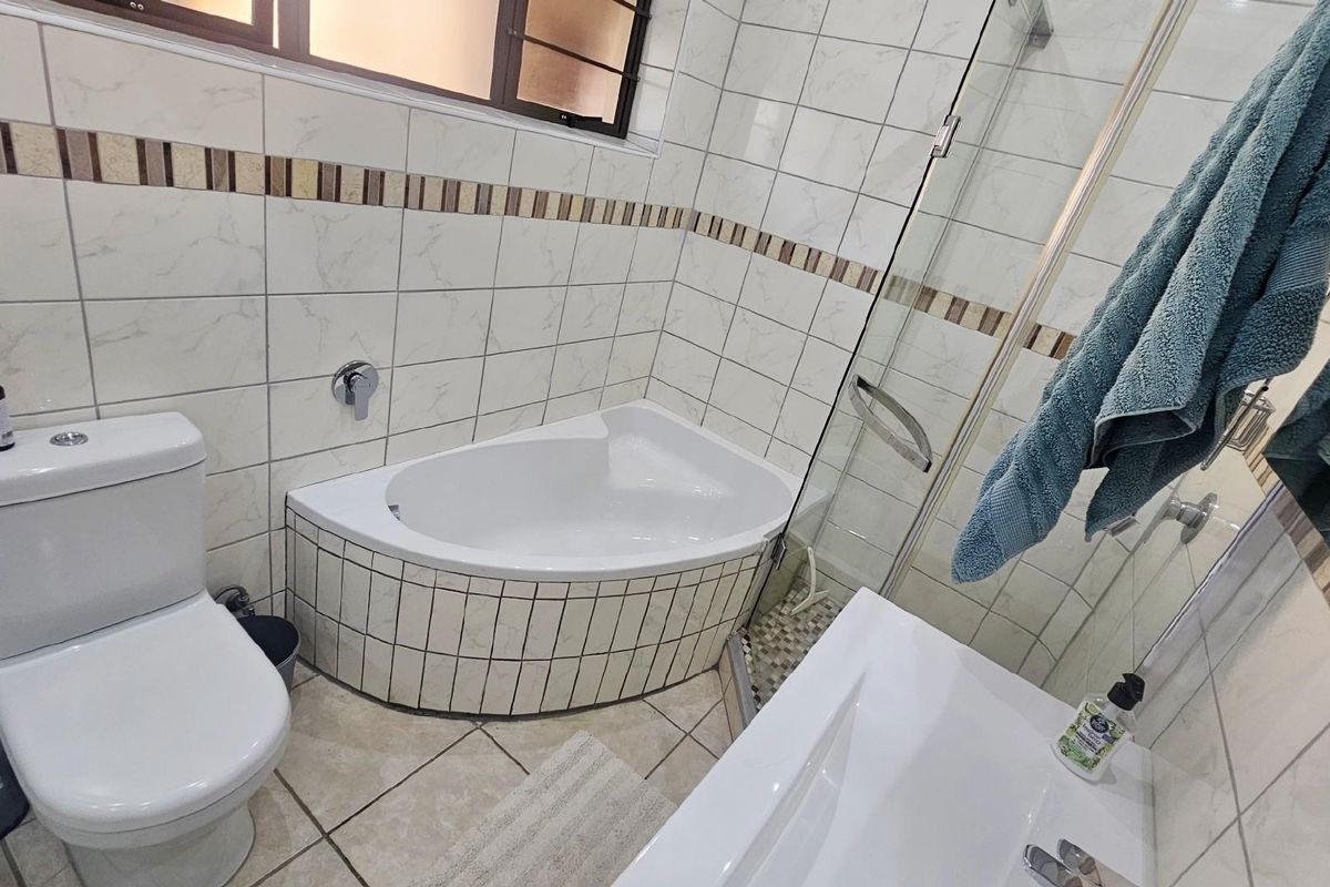A functional bathroom featuring a corner bathtub, a separate glass-enclosed shower, and tiled wall finishes with decorative border accents.