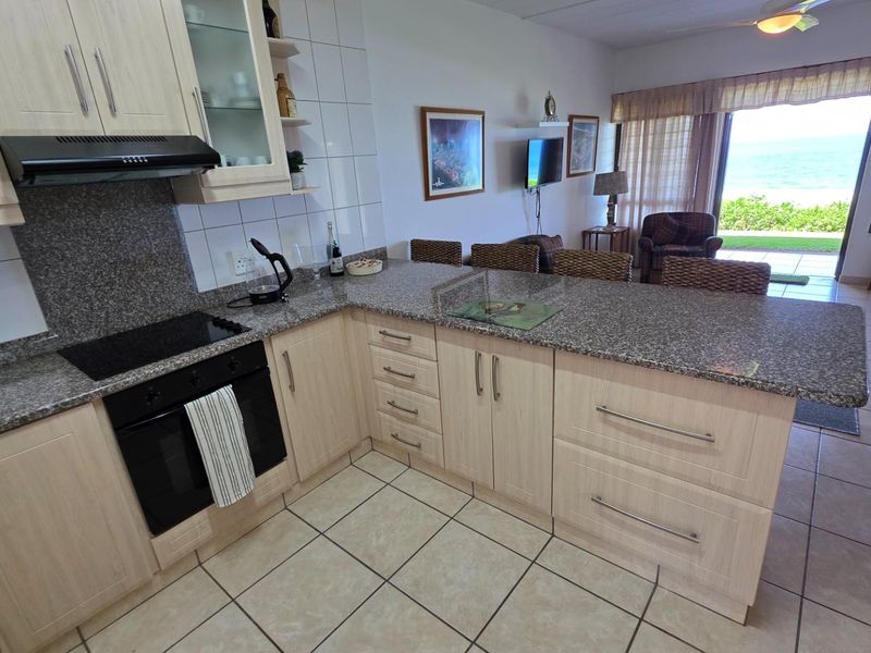 Open-plan kitchen featuring light wood cabinetry, granite countertops, and a built-in oven and hob, flowing into a living area with ocean views.