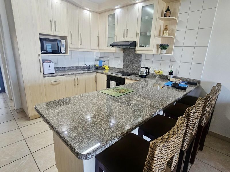 A functional kitchen featuring light wood cabinetry, granite countertops, a breakfast bar, built-in oven, hob, and extractor fan with tiled flooring.