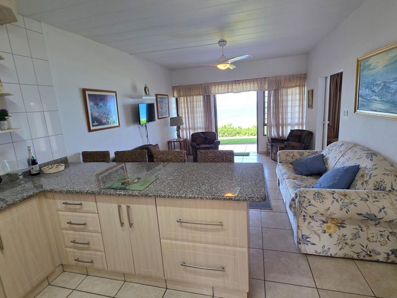 Open-plan living area featuring a functional kitchen with granite countertops, flowing into a lounge space with direct access to an outdoor patio.
