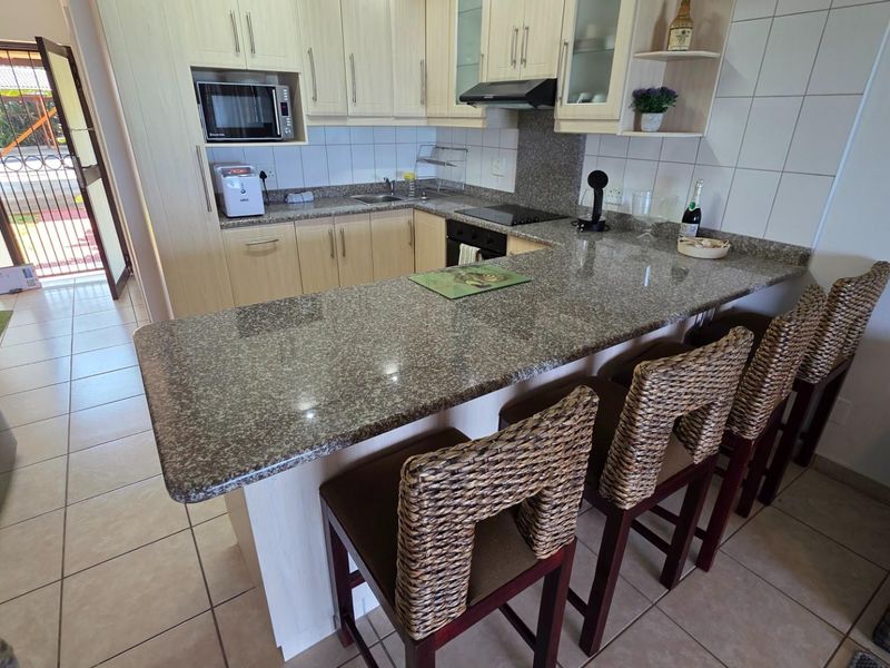 A functional kitchen featuring light-toned cabinetry, granite countertops, a breakfast bar, and tiled flooring, with direct access to an outdoor patio area.