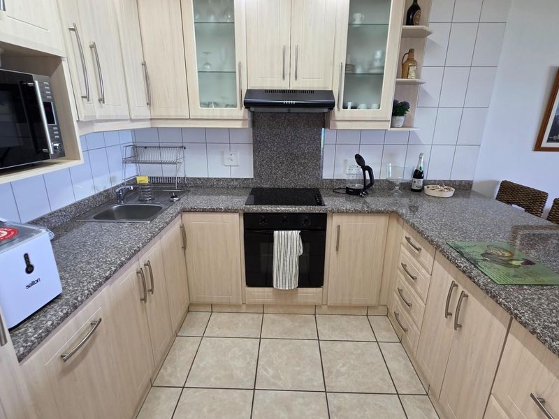 A functional kitchen featuring light wood cabinetry, granite countertops, a built-in oven, electric hob, extractor fan, and tiled flooring.